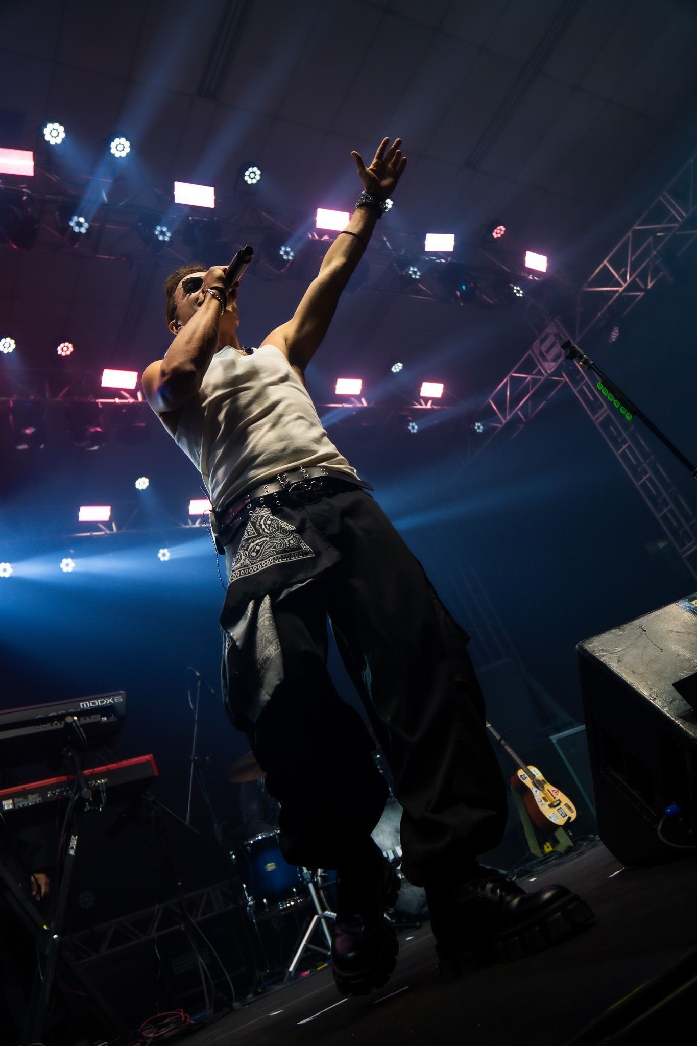 Um artista no palco segurando um microfone com um braço levantado sob holofotes brilhantes em uma casa de shows
