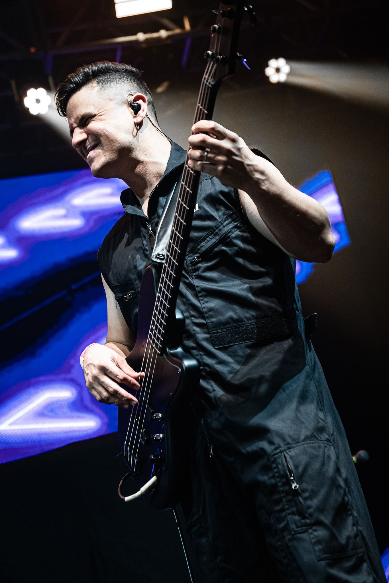 Um músico tocando baixo no palco sob holofotes brilhantes com um fundo neon azul desfocado.