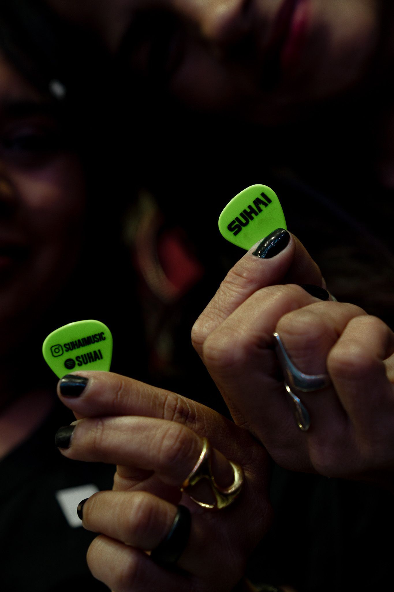 Duas mãos seguram palhetas de guitarra verde neon com os textos 