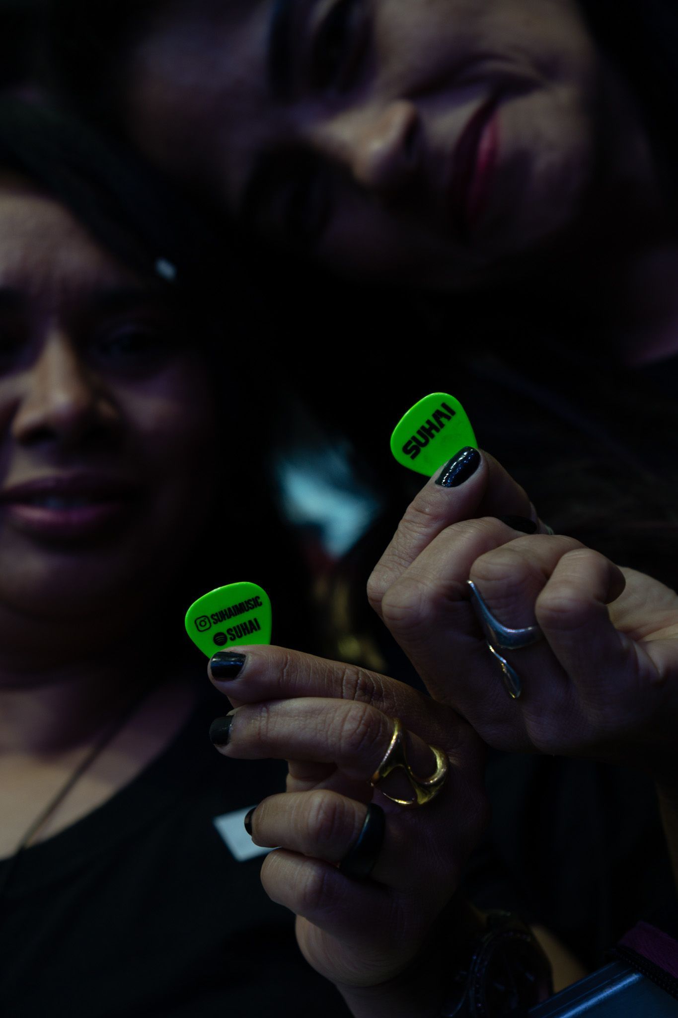 Duas pessoas segurando palhetas de guitarra verde-brilhante em um ambiente com pouca luz.