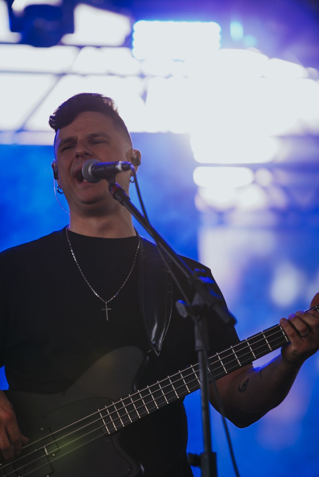Um músico cantando e tocando um baixo preto no palco com um fundo de luz azul.