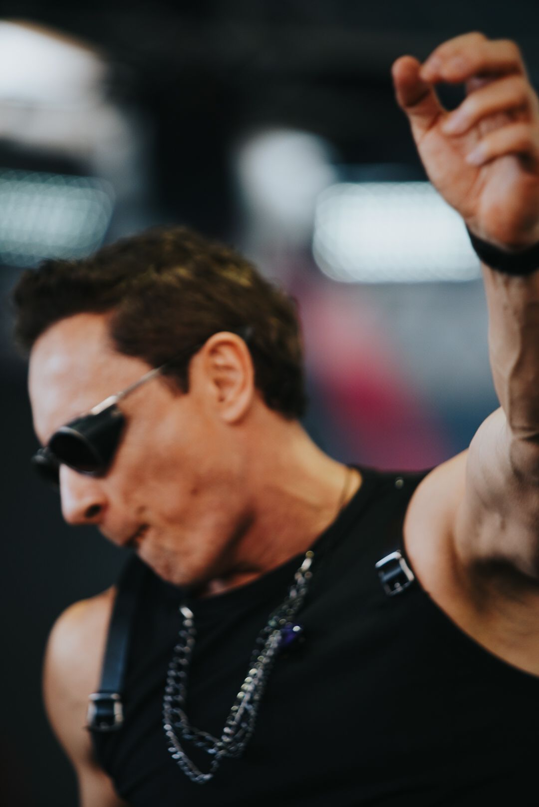 Um artista usando óculos escuros e colete preto levanta o braço, se apresentando no palco.