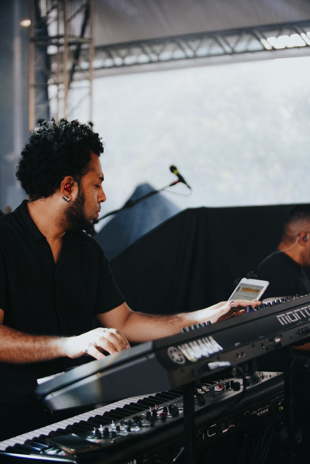Um artista tocando teclado em um palco; vestindo preto, com expressão concentrada.
