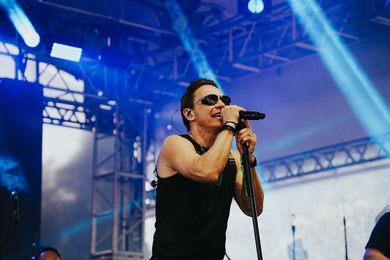 Um artista de óculos escuros cantando em um microfone em um palco com iluminação azul.