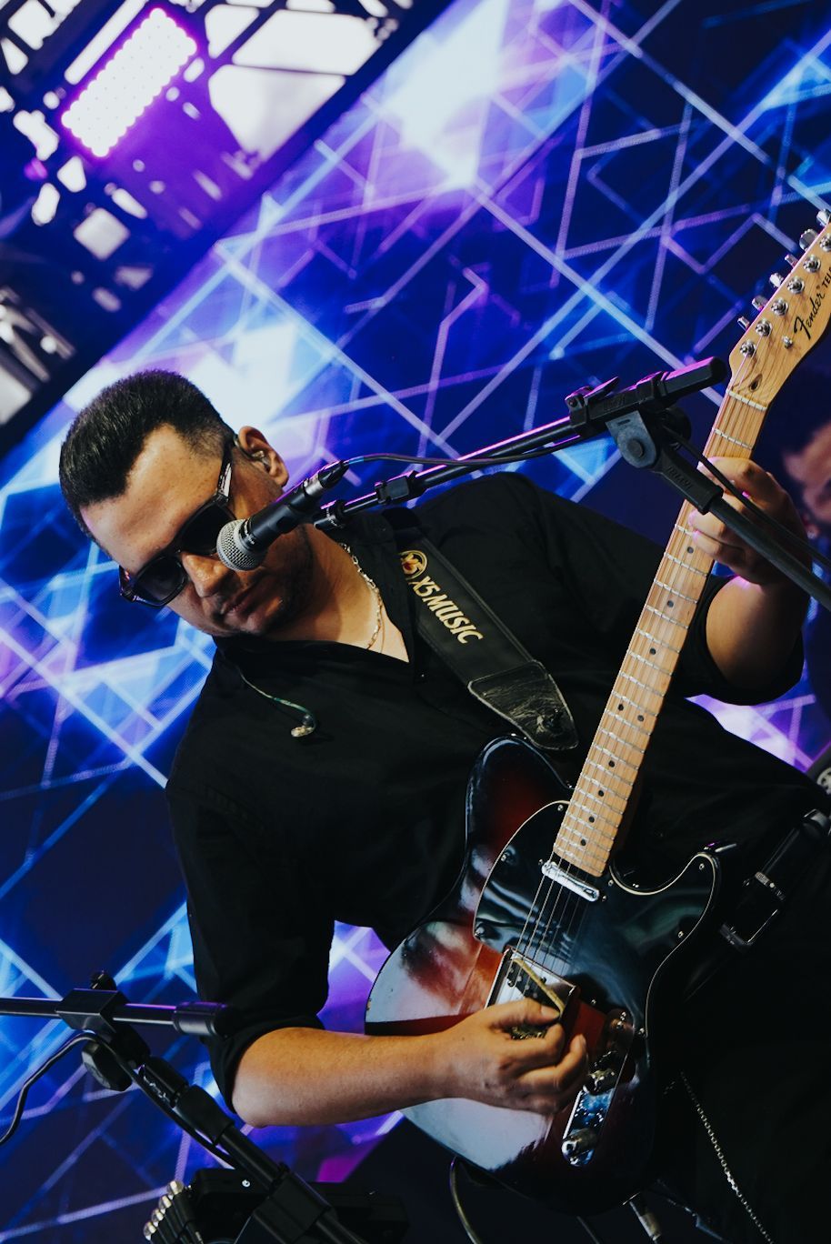Um artista tocando guitarra elétrica no palco com um fundo de luz azul.