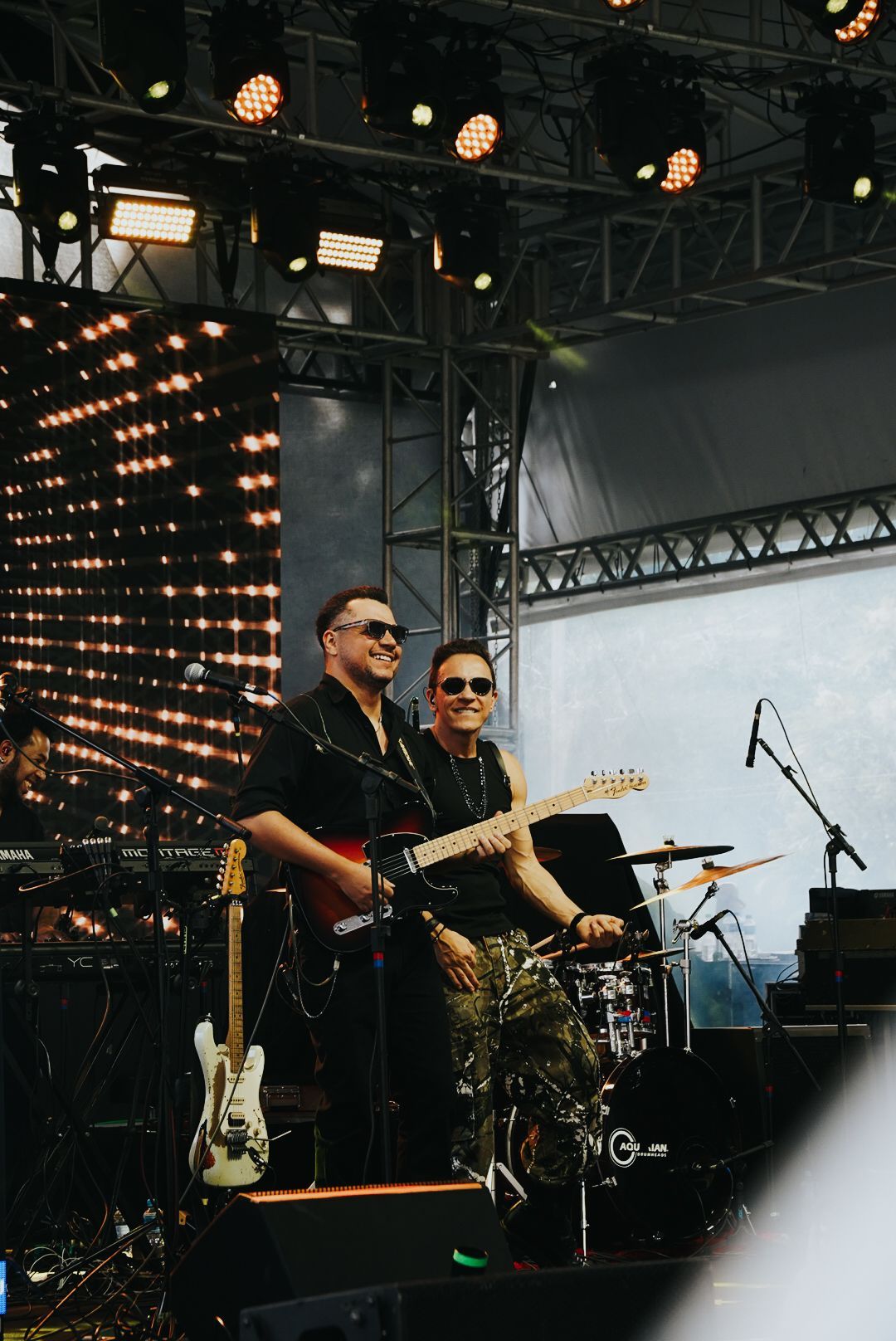 Dois artistas com guitarras se apresentando no palco sob luzes de palco.