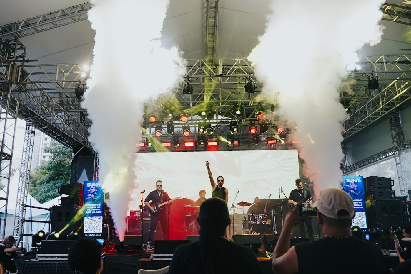 Banda se apresentando no palco em show ao ar livre com efeitos de fumaça.