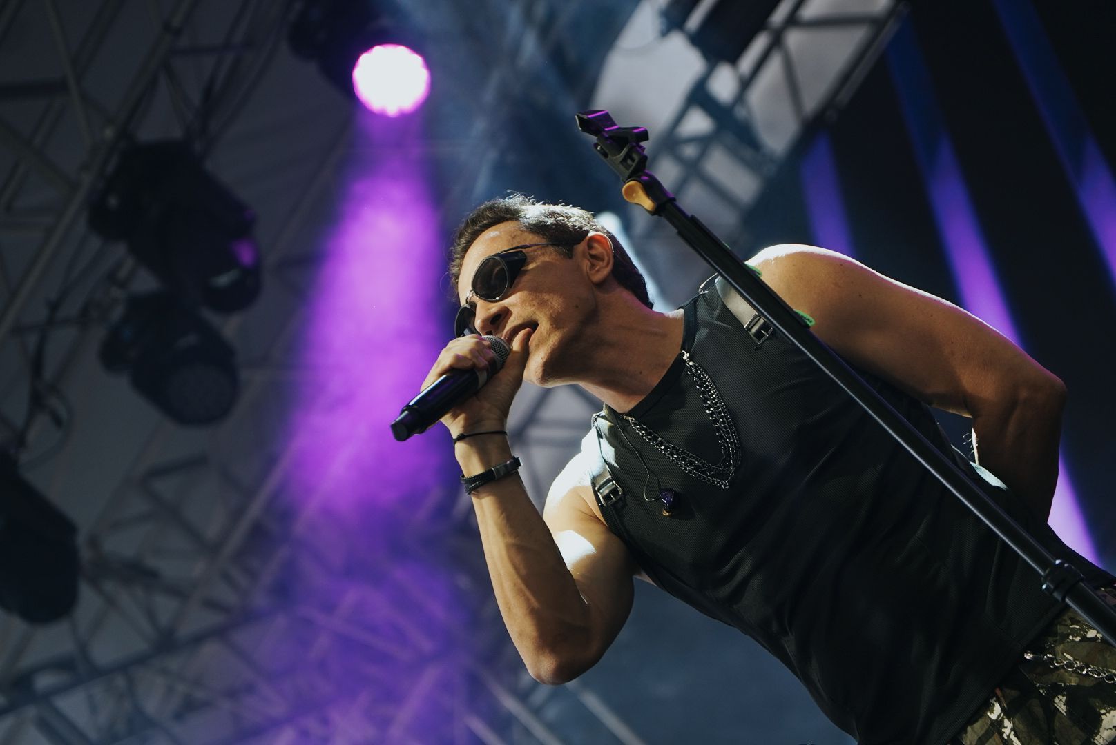 Um artista cantando ao microfone no palco, segurando um violão. Iluminação roxa e cenário de fundo roxo.