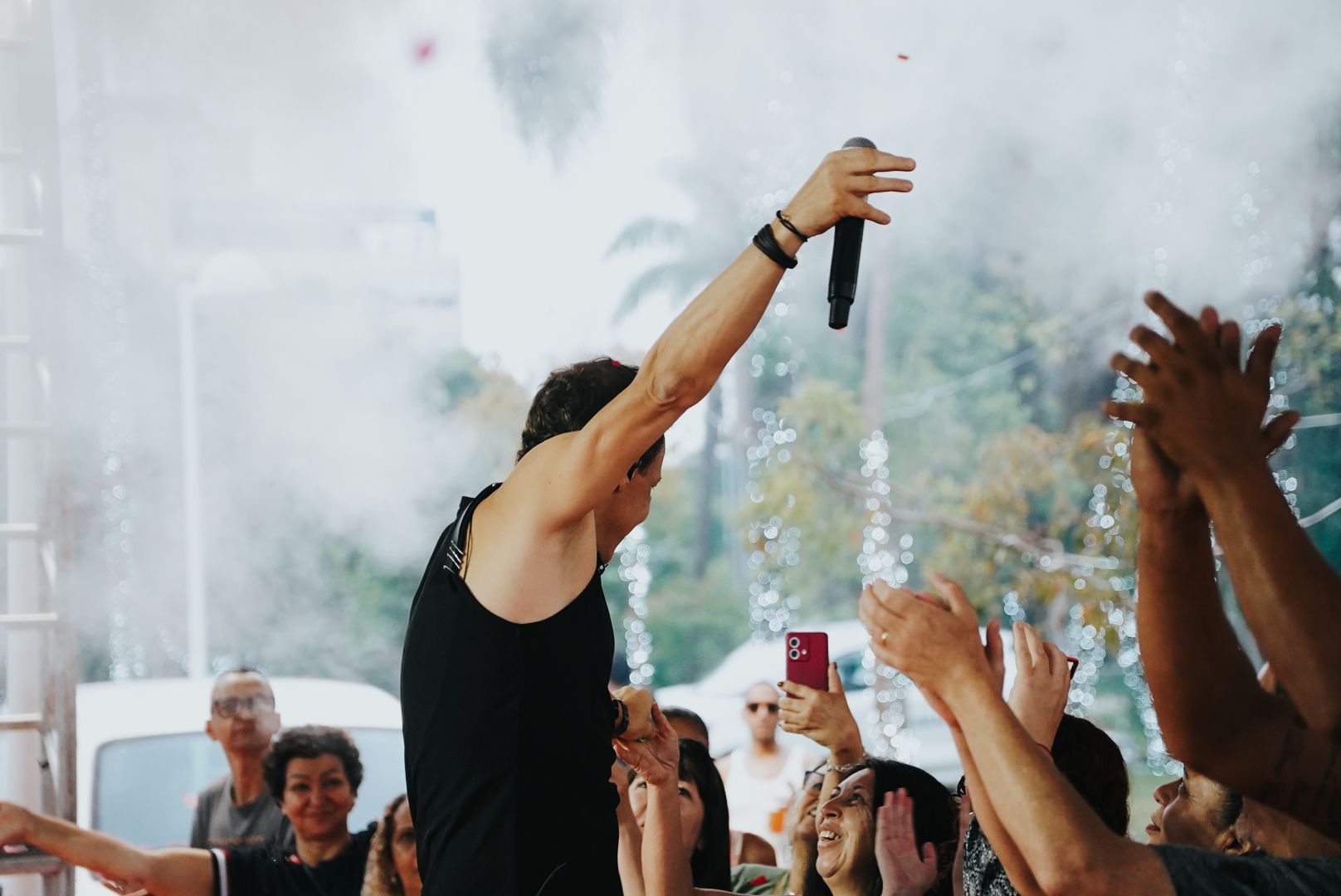 Cantor no palco, levantando o microfone, plateia aplaudindo com efeito de fumaça. Apresentação ao ar livre.