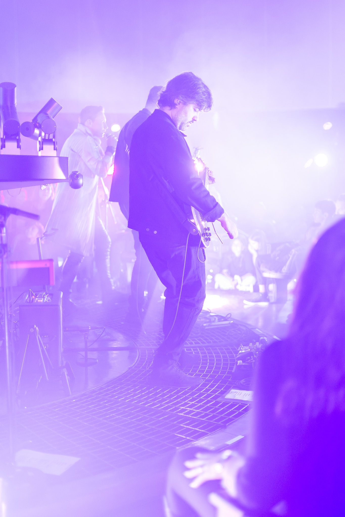 Um músico está no palco se apresentando, banhado por uma luz roxa brilhante e difusa.