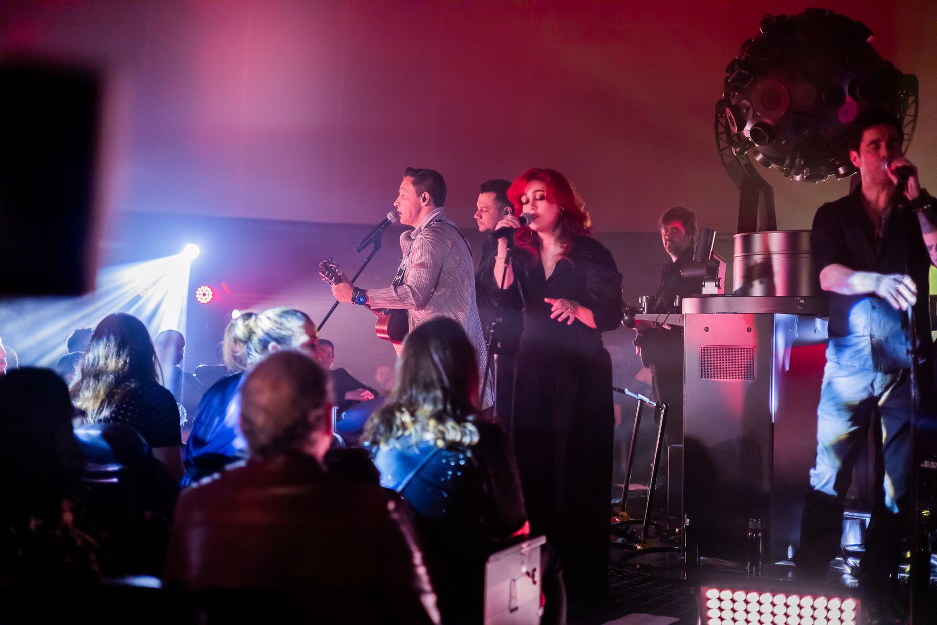 Um grupo musical se apresenta em um palco com pouca iluminação, iluminado apenas por holofotes brilhantes e equipamentos.