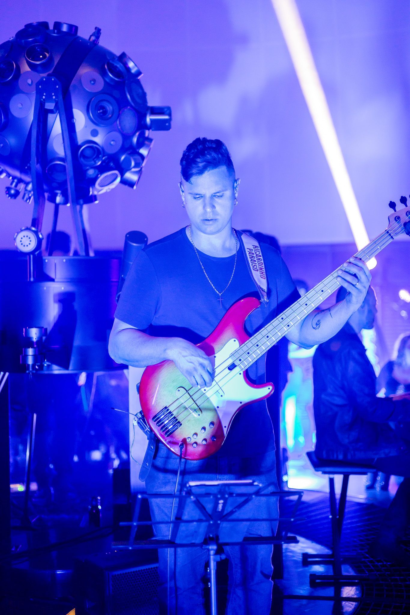 Um artista toca uma guitarra elétrica no palco sob iluminação azul, em frente a uma grande bola de discoteca esférica.