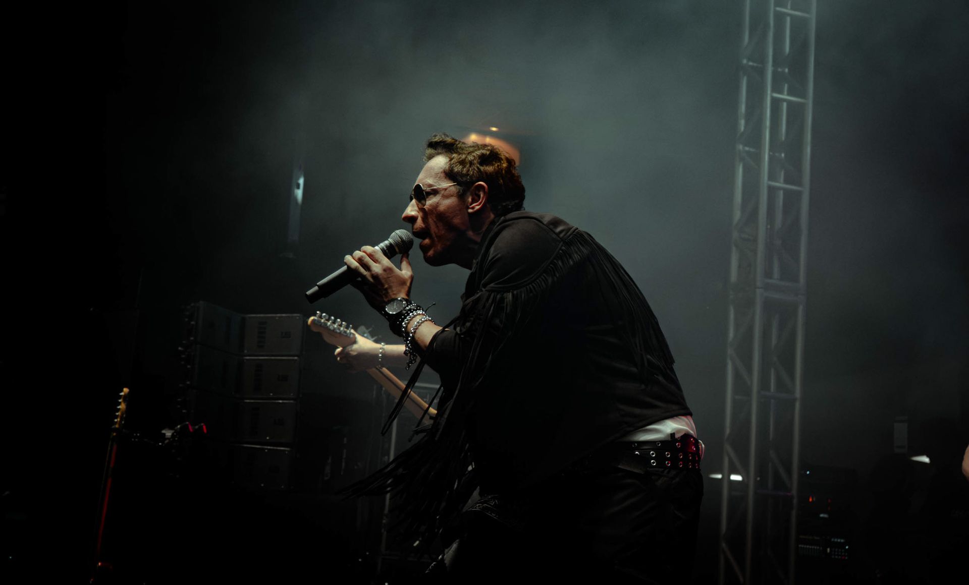 Uma pessoa vestida de escuro canta em um microfone em um palco pouco iluminado