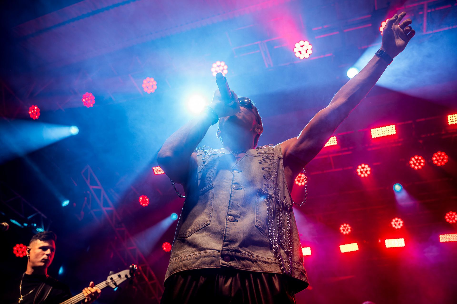 Uma pessoa cantando em um microfone no palco, iluminada por holofotes azuis e vermelhos brilhantes