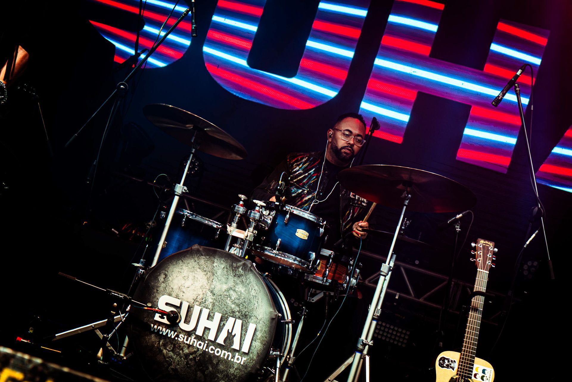 Um baterista está sentado atrás de uma bateria com a inscrição 