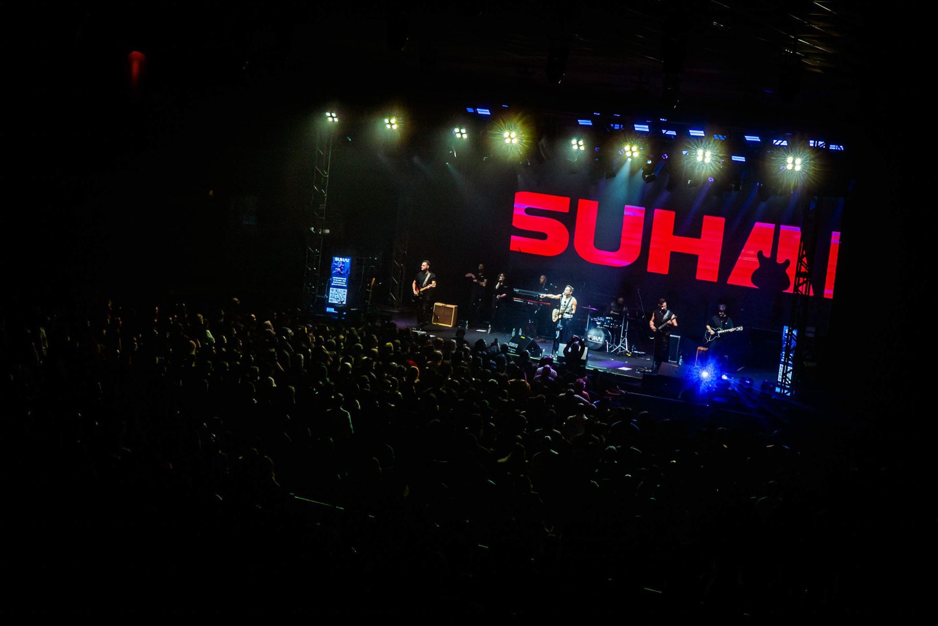 Uma banda se apresenta em com um grande letreiro vermelho brilhante com a palavra 