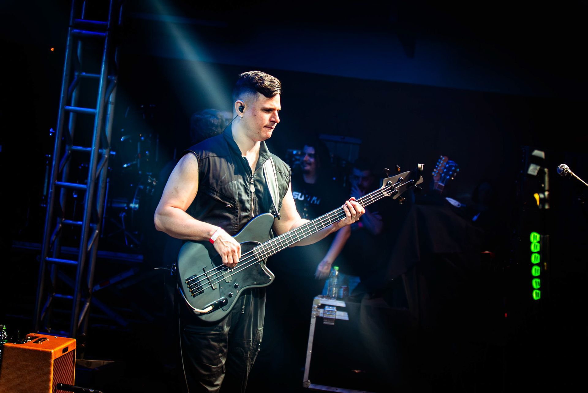 Um artista no palco tocando um baixo elétrico escuro sob um holofote brilhante em um local com pouca luz.