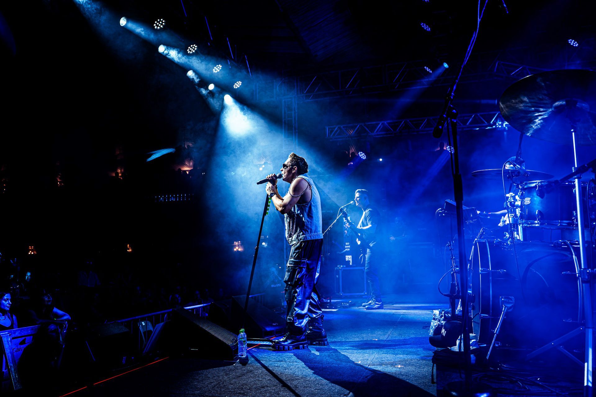 Um músico cantando em um microfone em um palco repleto de luzes azuis dramáticas e névoa.