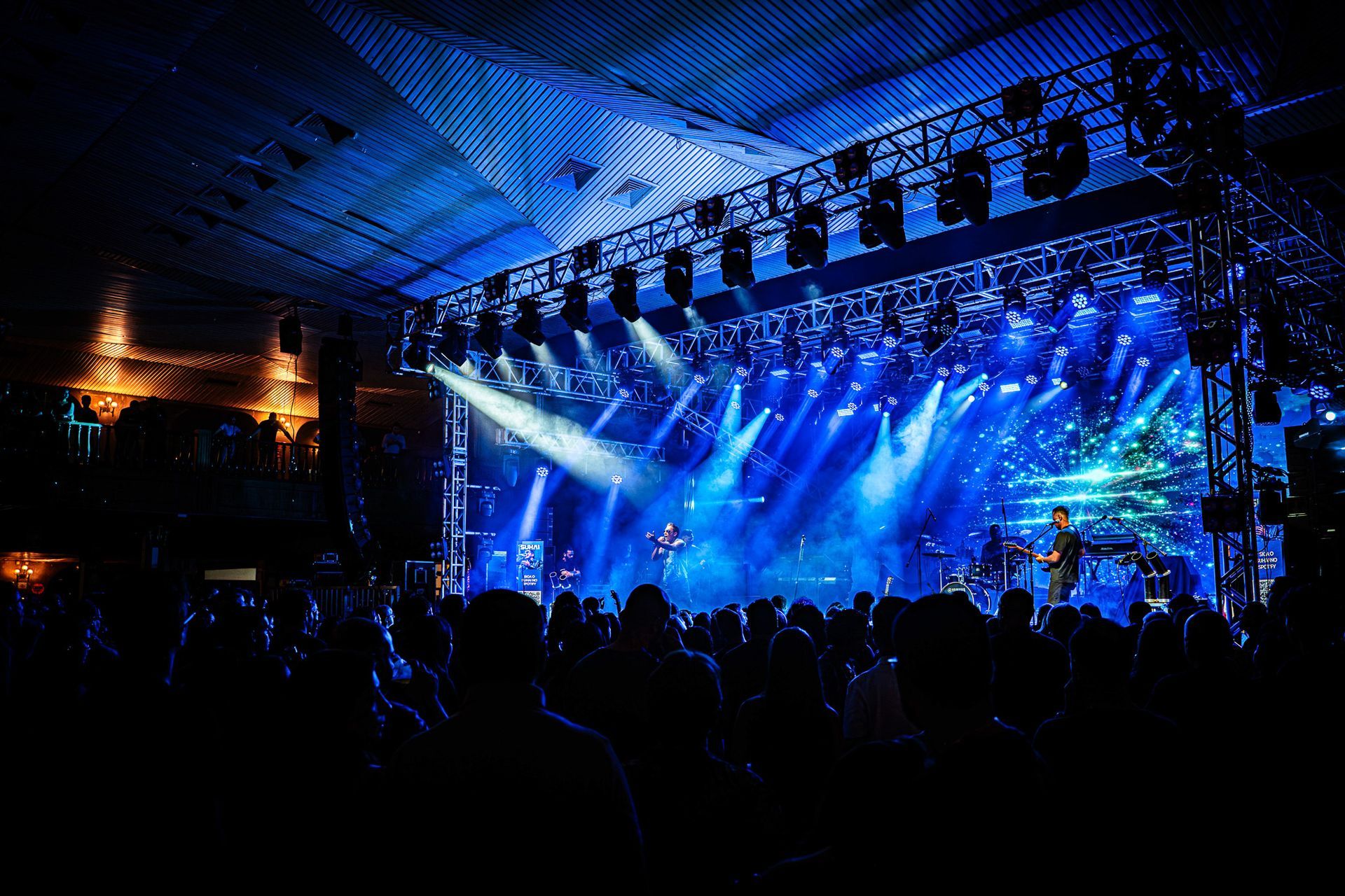 Um palco de concerto ao vivo, com uma multidão em silhueta assistindo à apresentação.