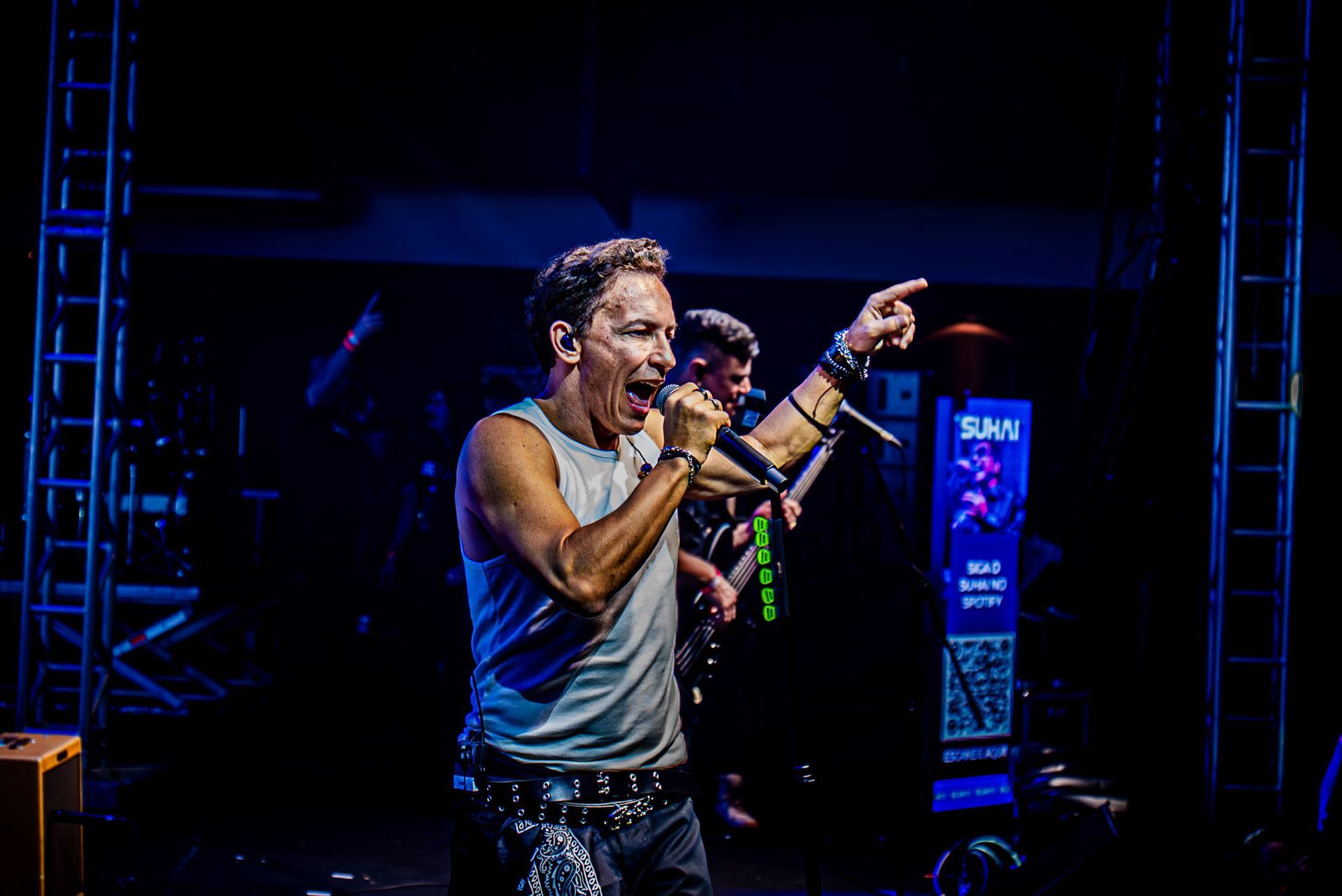 Um artista canta em um microfone no palco de um concerto, apontando para o lado com uma das mãos.