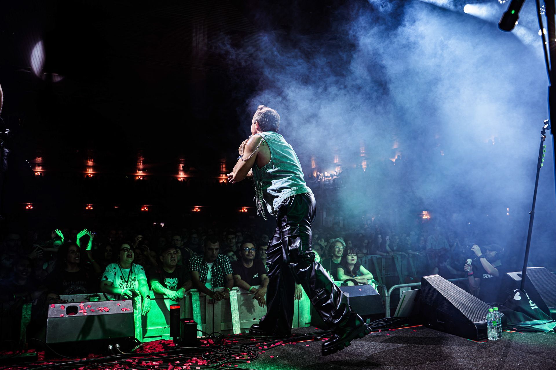 Um artista está em um palco banhado por luzes azuis e névoa, de frente para uma plateia em uma casa de shows com pouca luz.