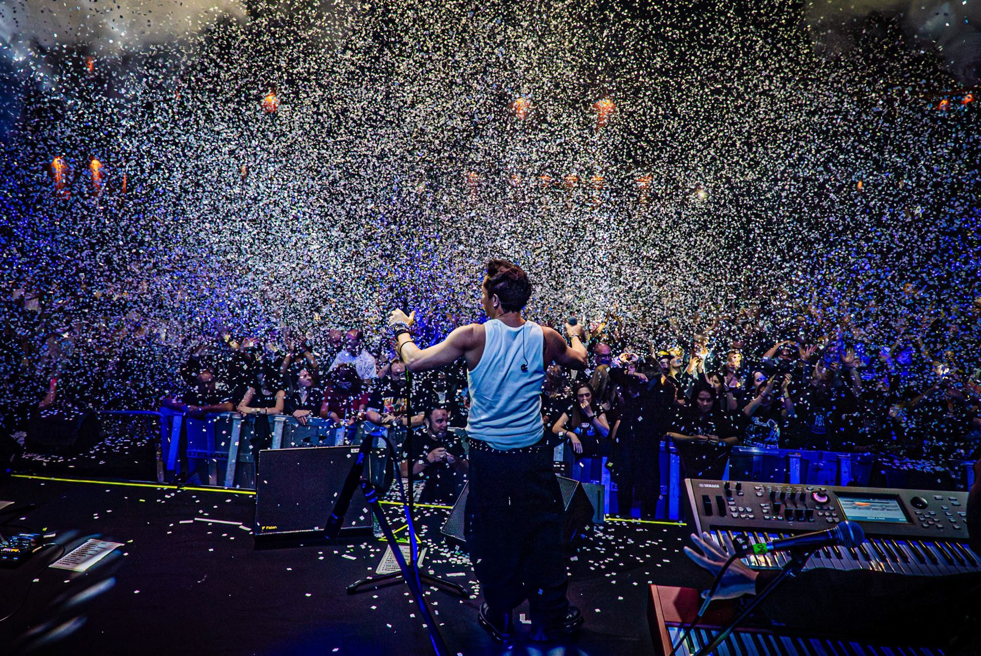 Um artista no palco encara uma grande plateia durante um show enquanto uma enorme chuva de confete branco cai sobre ele.