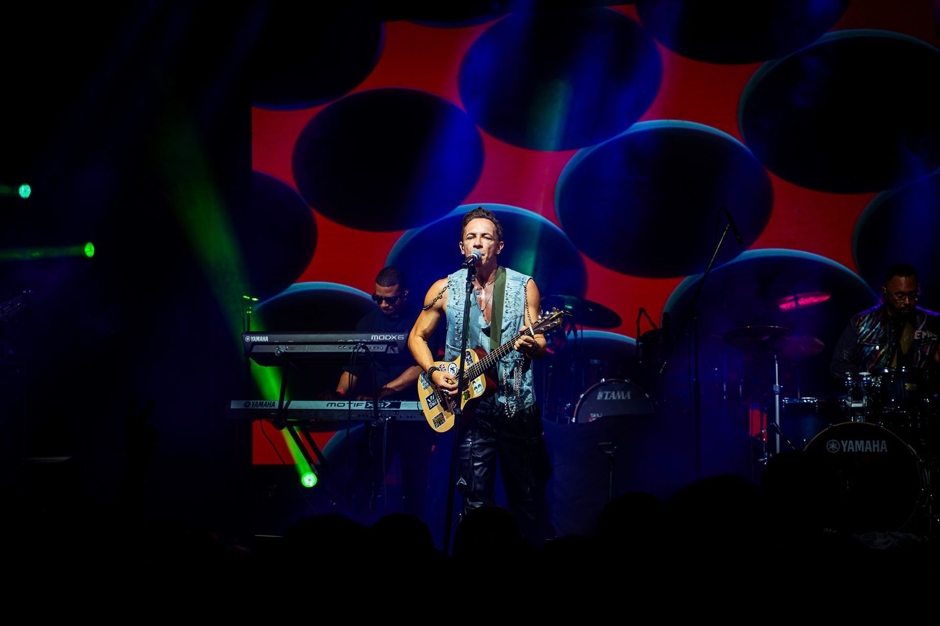 Um artista canta enquanto toca guitarra em um palco com grandes formas circulares escuras projetadas