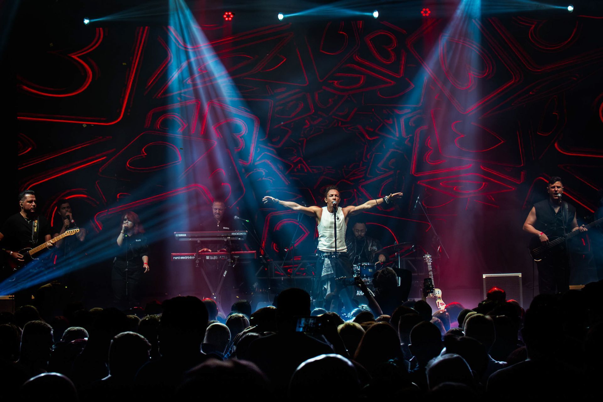 O vocalista principal está no centro do palco com os braços estendidos, apresentando-se para uma plateia ao vivo.