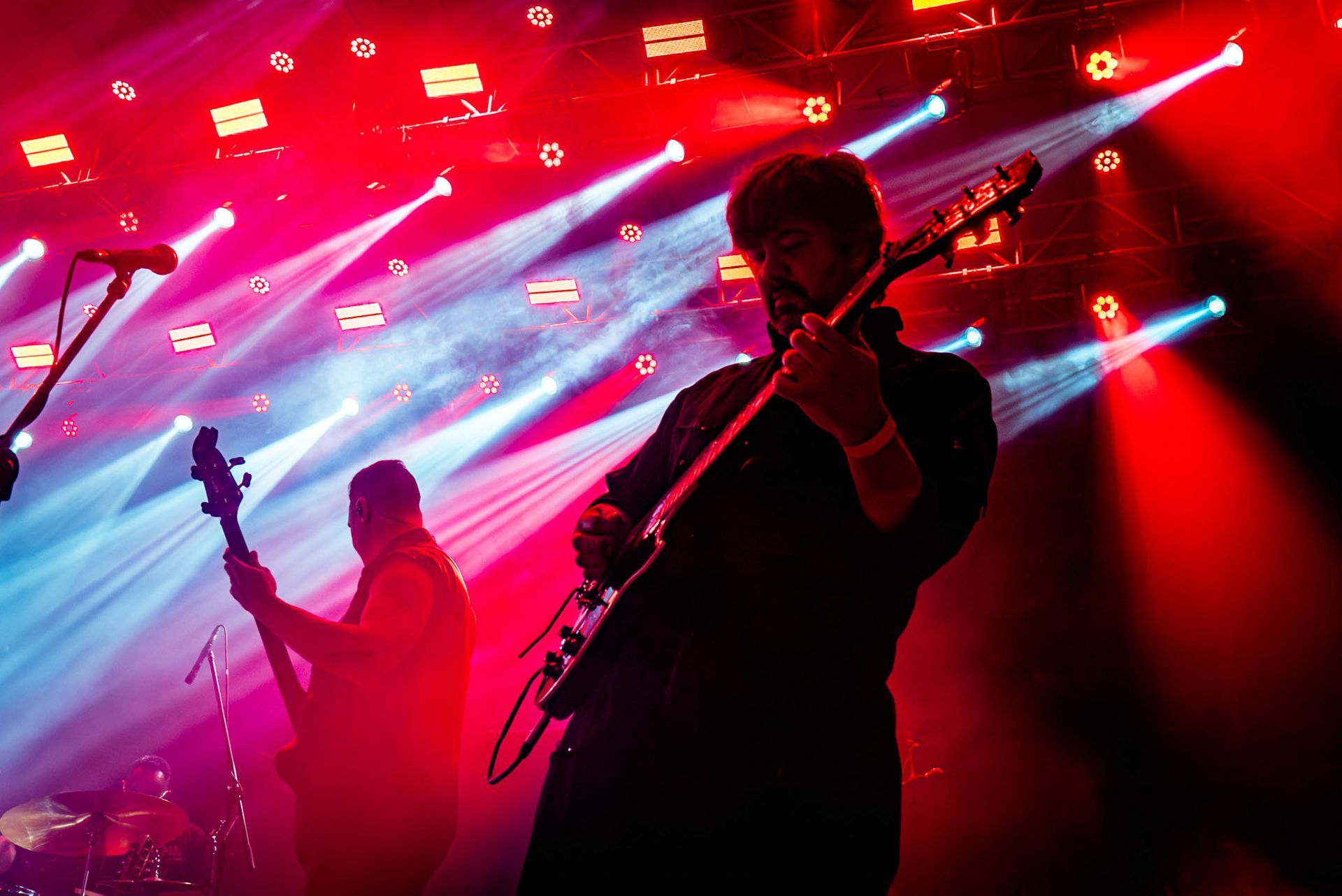 Dois músicos se apresentam em um palco iluminado por holofotes de concerto vermelhos e azuis brilhantes.