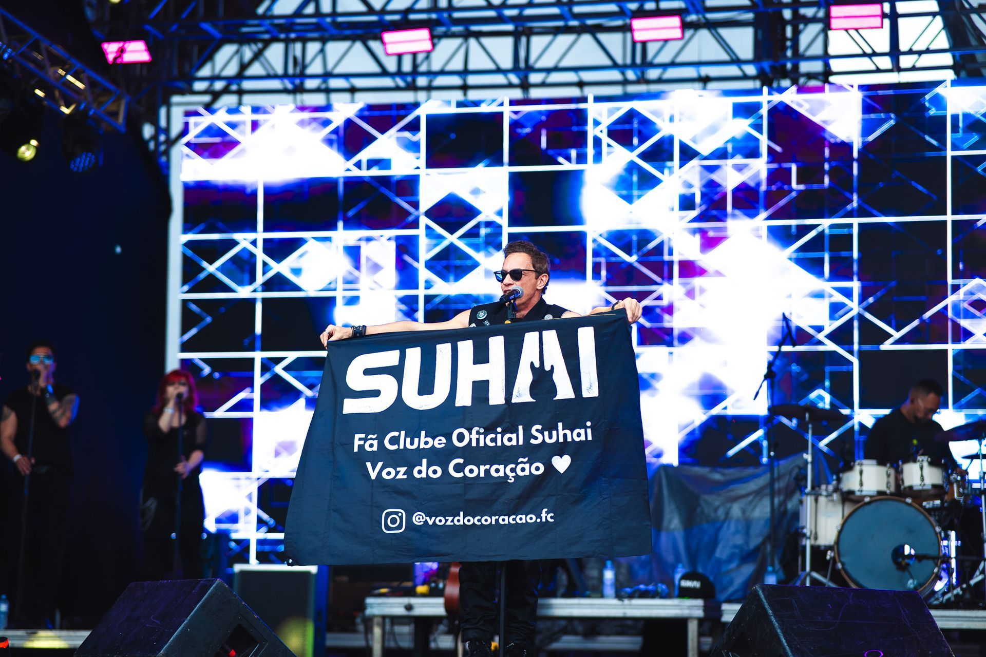 Cantor no palco segurando uma faixa com os dizeres 