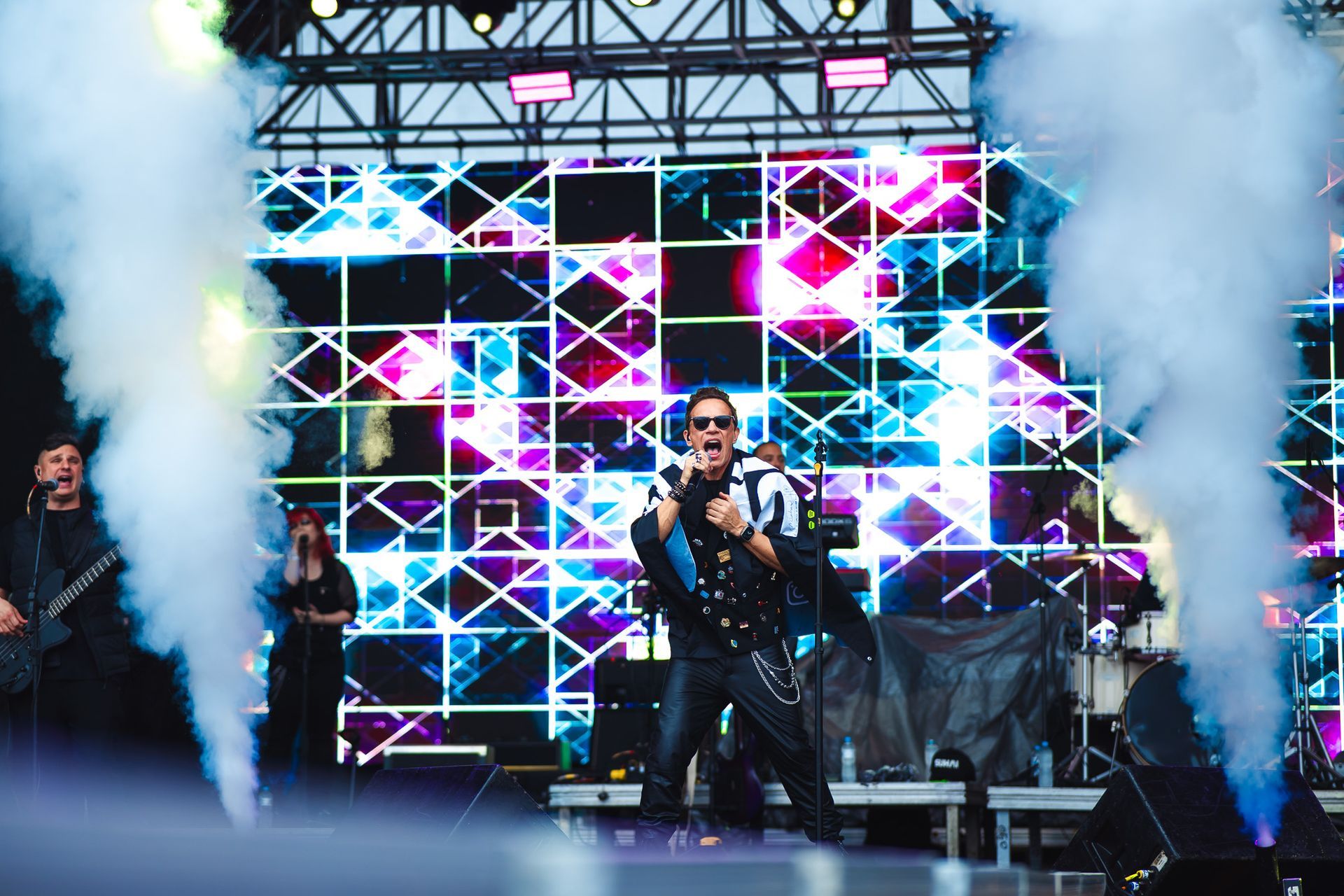 Banda se apresentando no palco com luzes coloridas e fumaça.