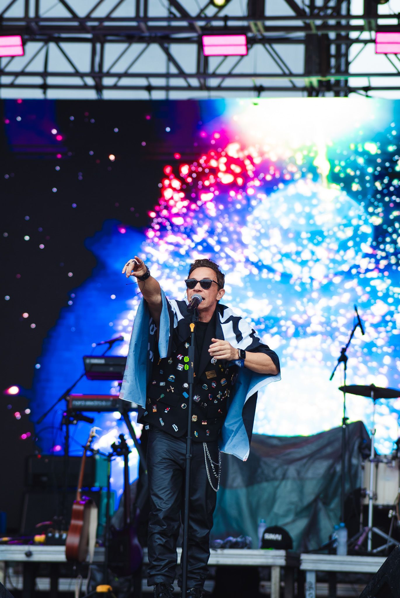 Um artista cantando e apontando durante um show. O palco está iluminado com luzes coloridas. 