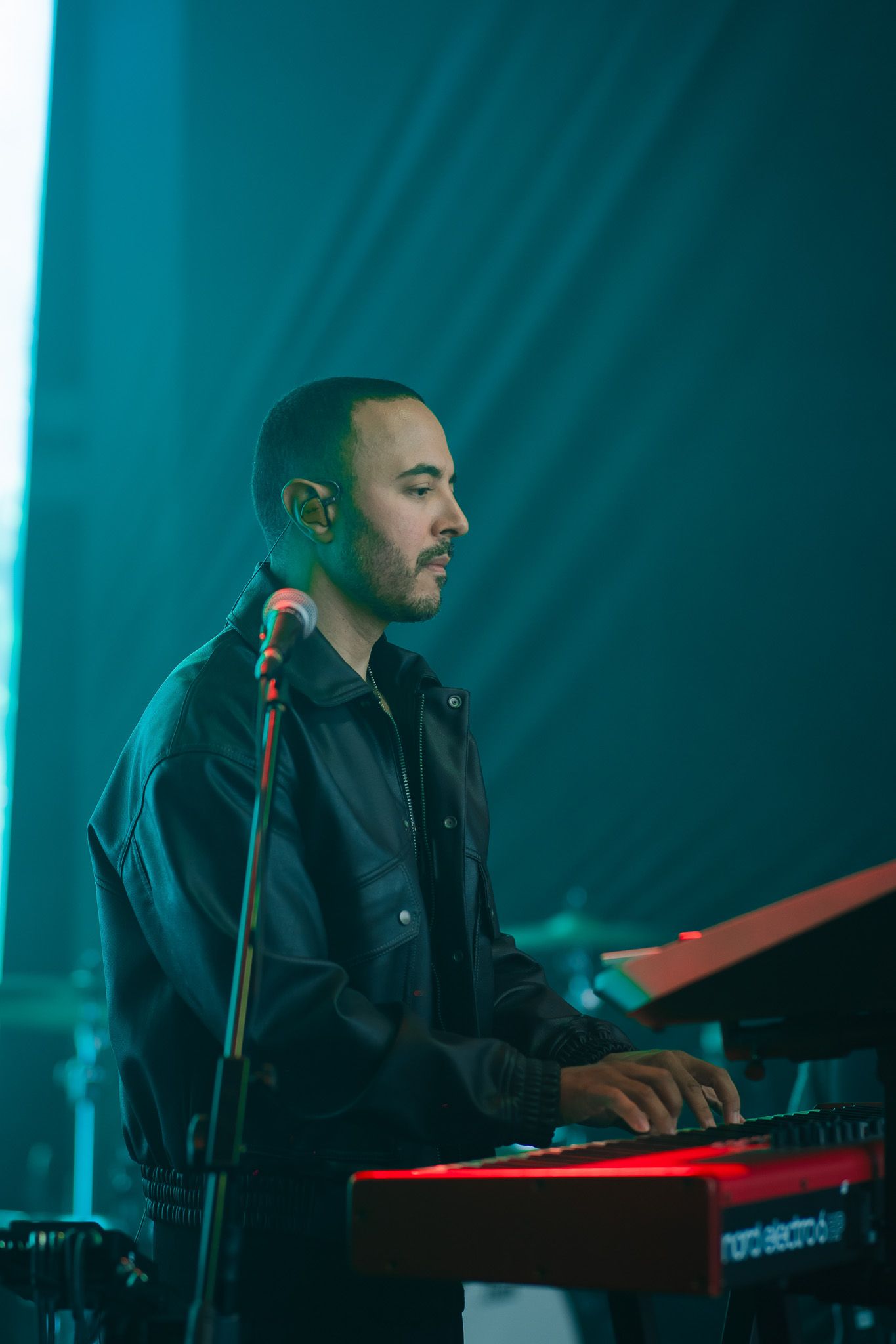 Um artista tocando teclado no palco, iluminado por luz azul.