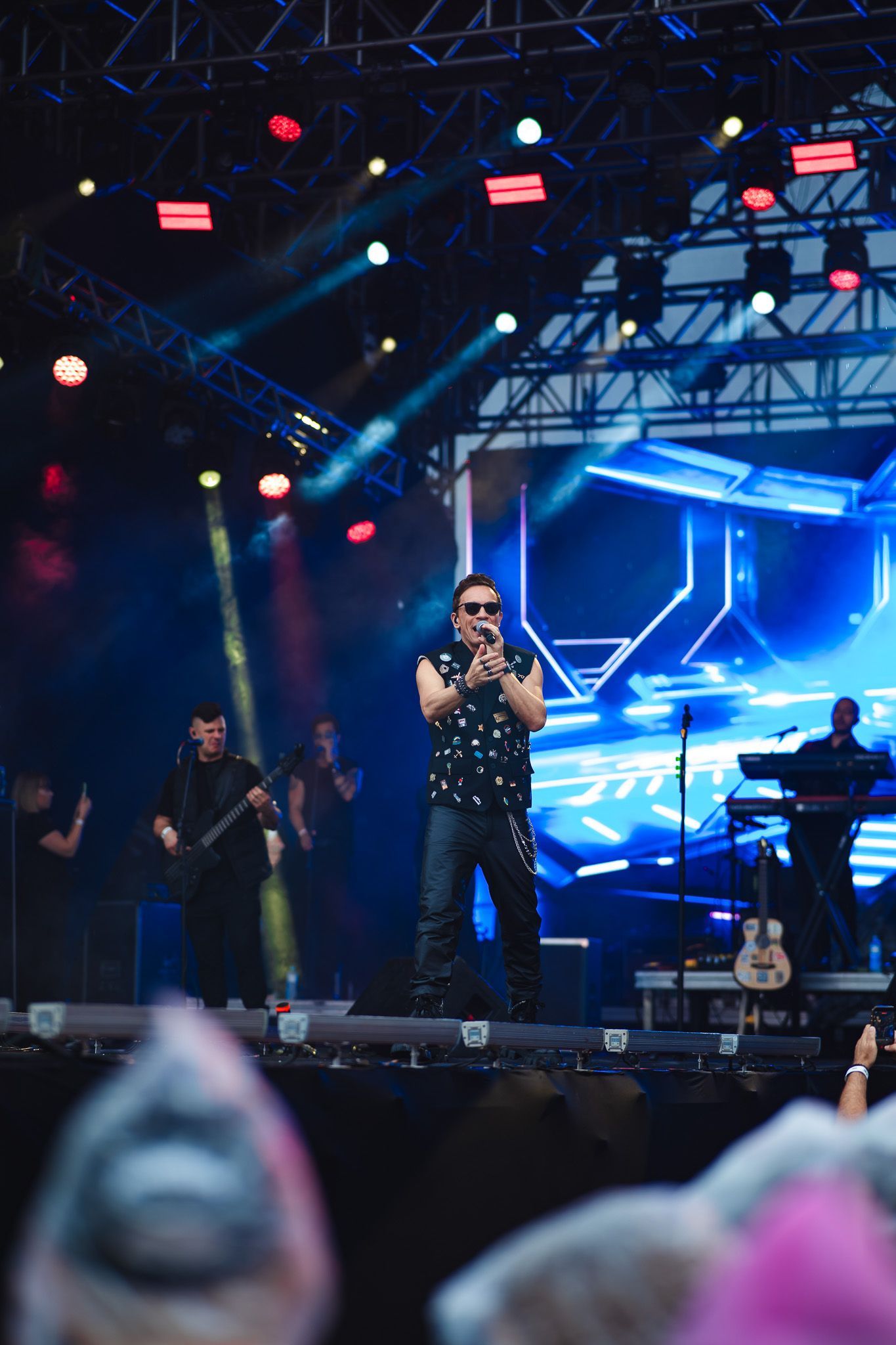 Um artista cantando no palco com a banda, palco iluminado com luzes azuis e vermelhas.