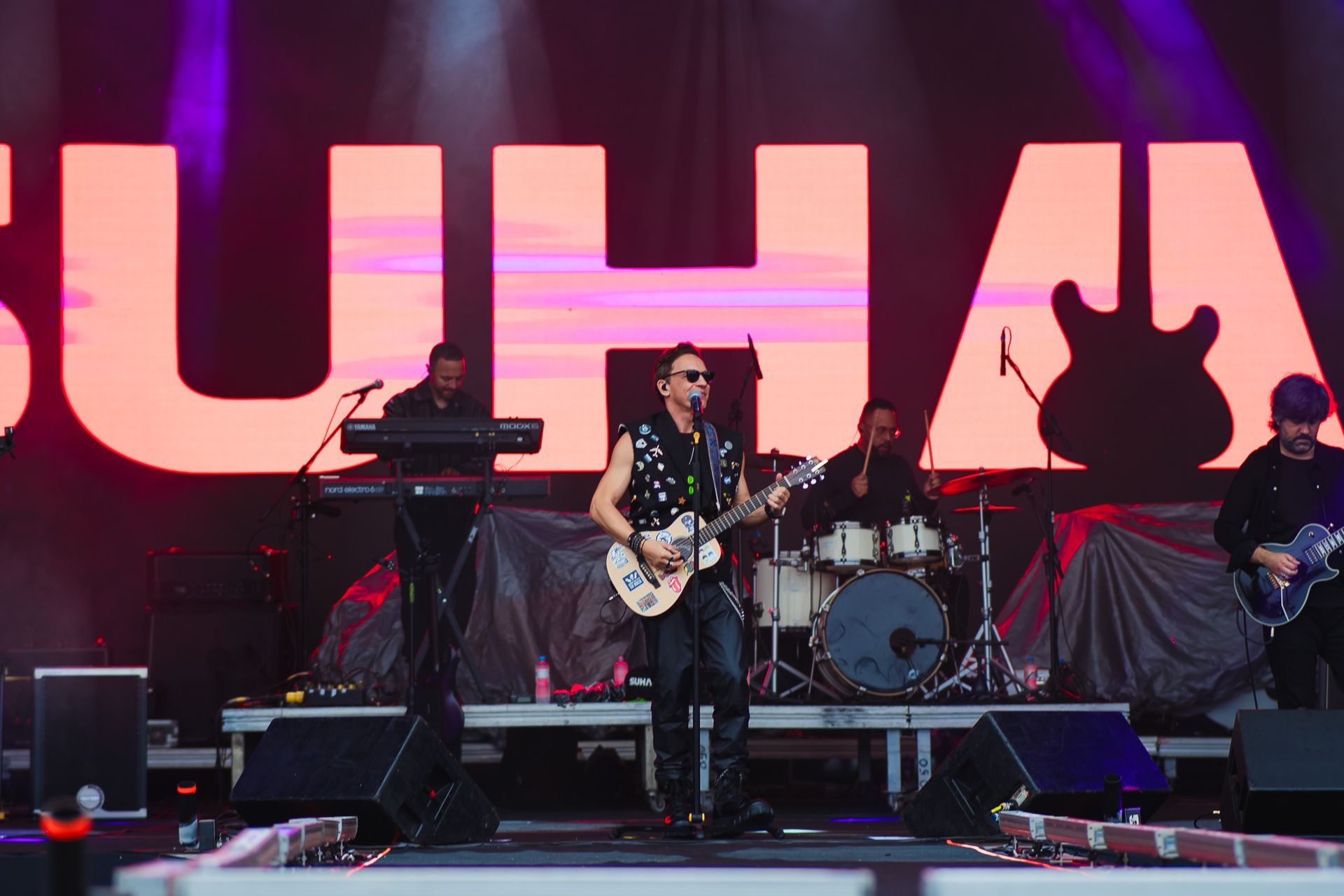 Banda se apresentando no palco de um festival de música sob uma placa da SUHAI.
