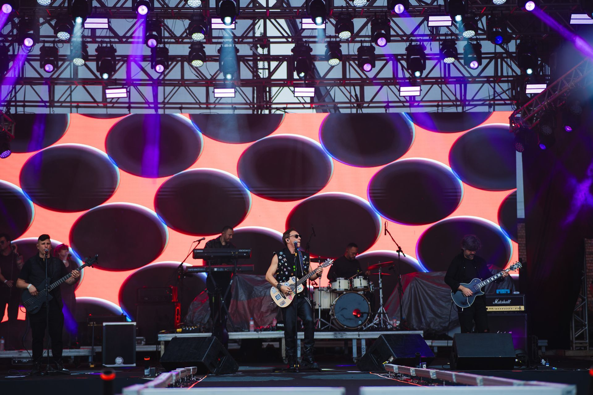 Banda se apresentando no palco com um telão ao fundo exibindo círculos pretos.