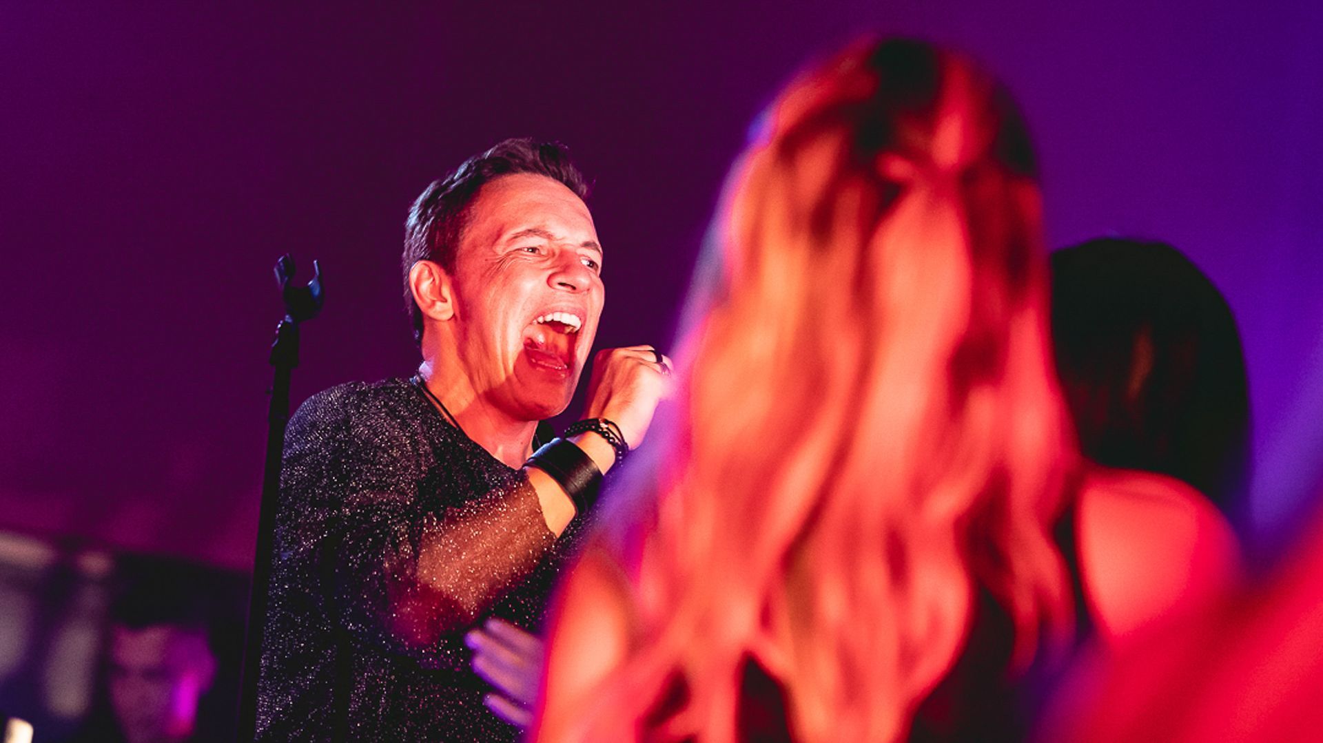 Um artista cantando com paixão em um microfone no palco, iluminada por uma vibrante luz vermelha.