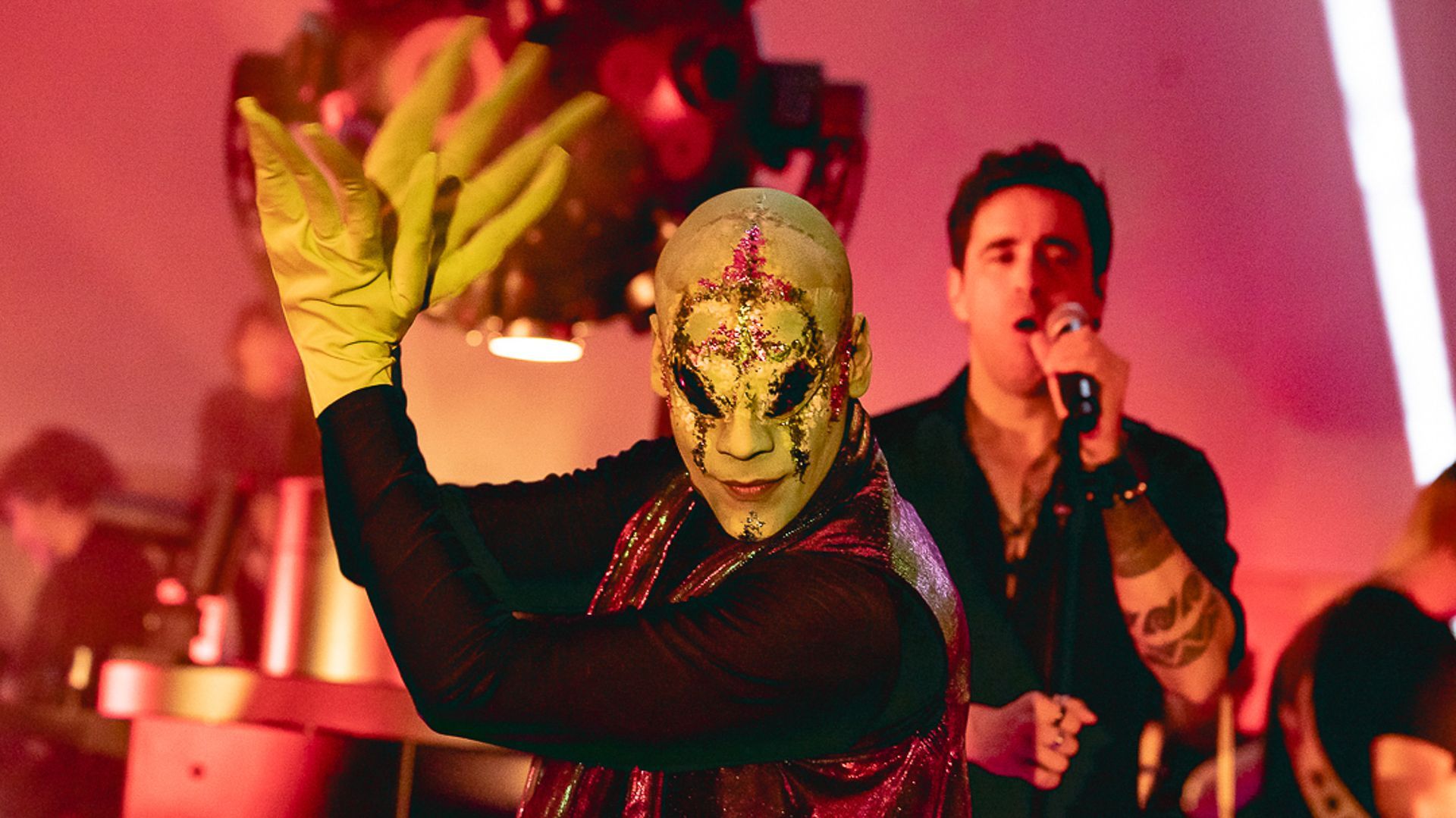 Um artista usando uma máscara ornamentada e pálida e luvas amarelas posa