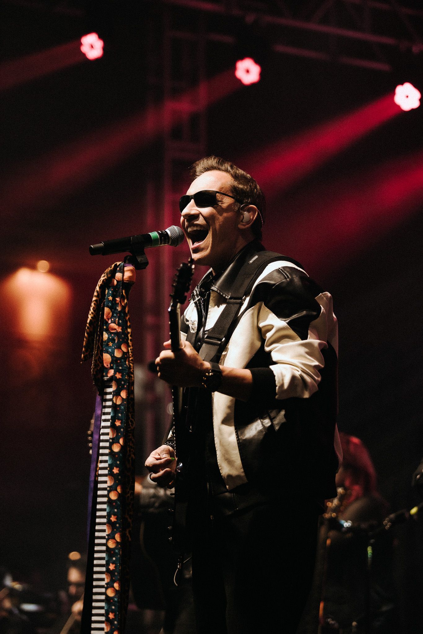 Um artista cantando e tocando violão no palco sob luzes vermelhas.