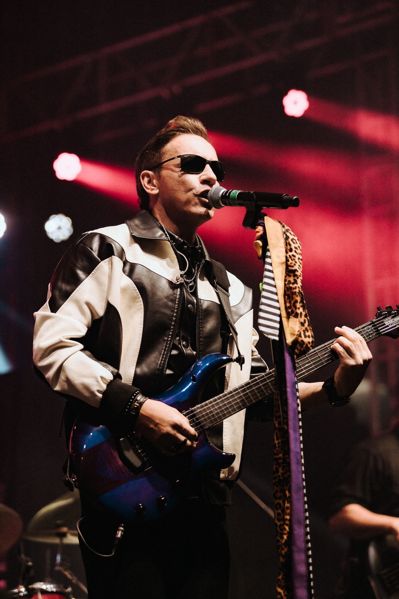 Um artista de óculos escuros tocando guitarra no palco com microfone.