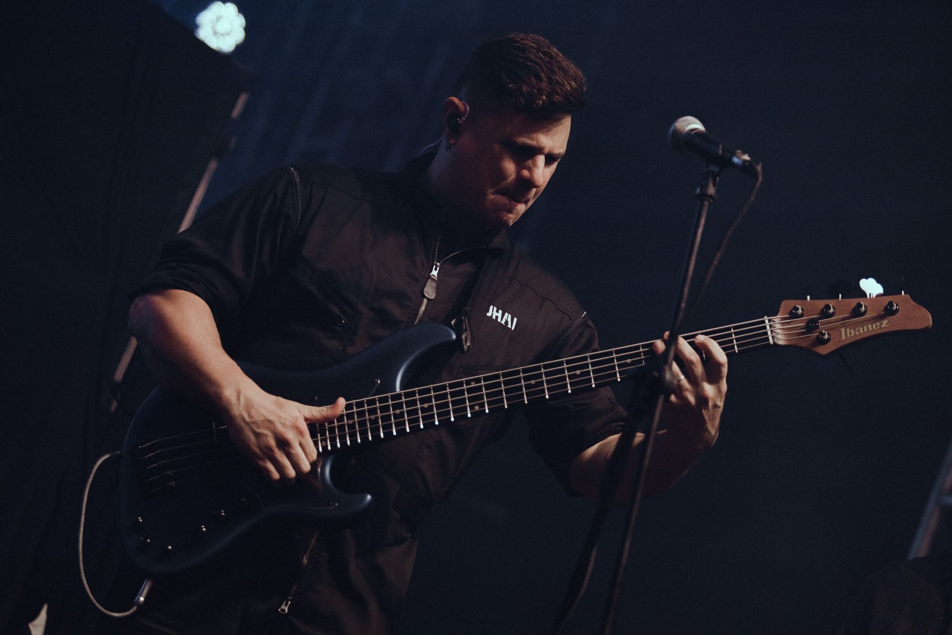 Um músico tocando baixo no palco, iluminado com luzes azuis e brancas.