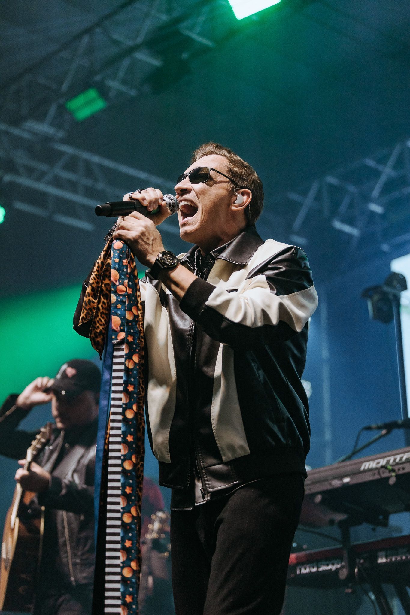 Cantor de óculos escuros e lenço estampado cantando no palco.