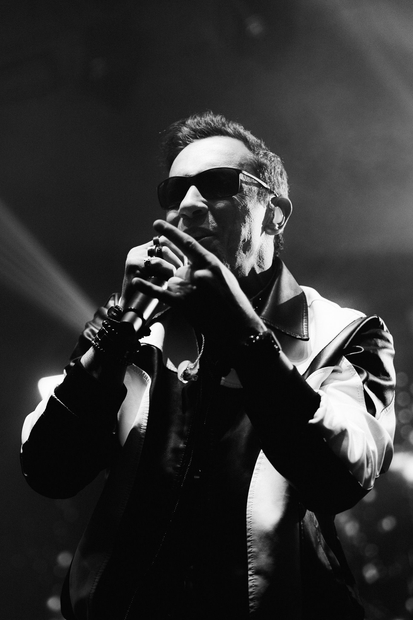 Um artista de óculos escuros segurando um microfone, se apresentando no palco.