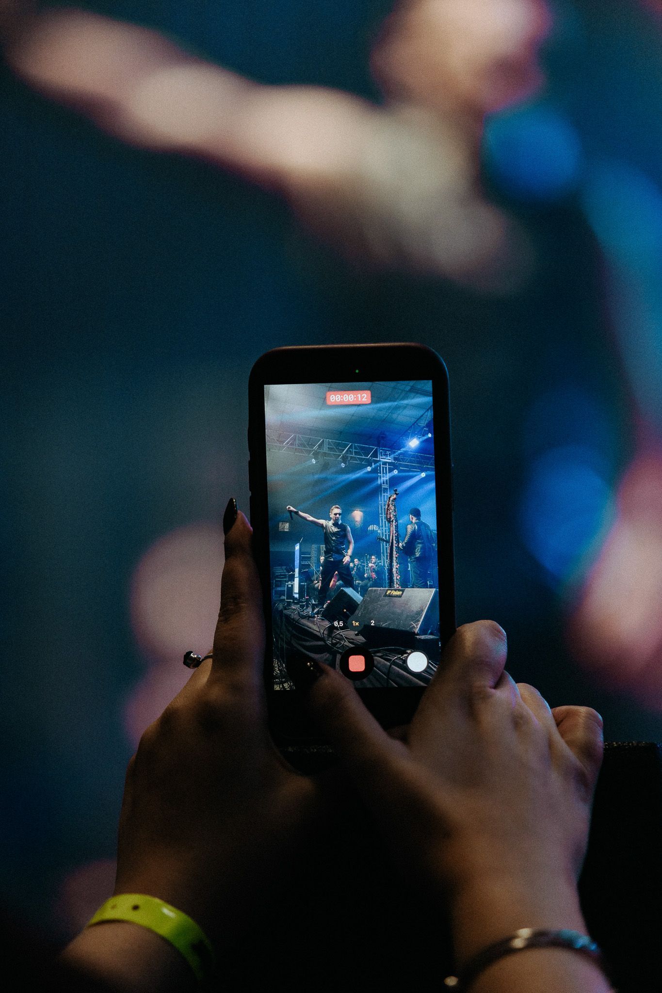 Mãos segurando um telefone enquanto gravam um show no palco.