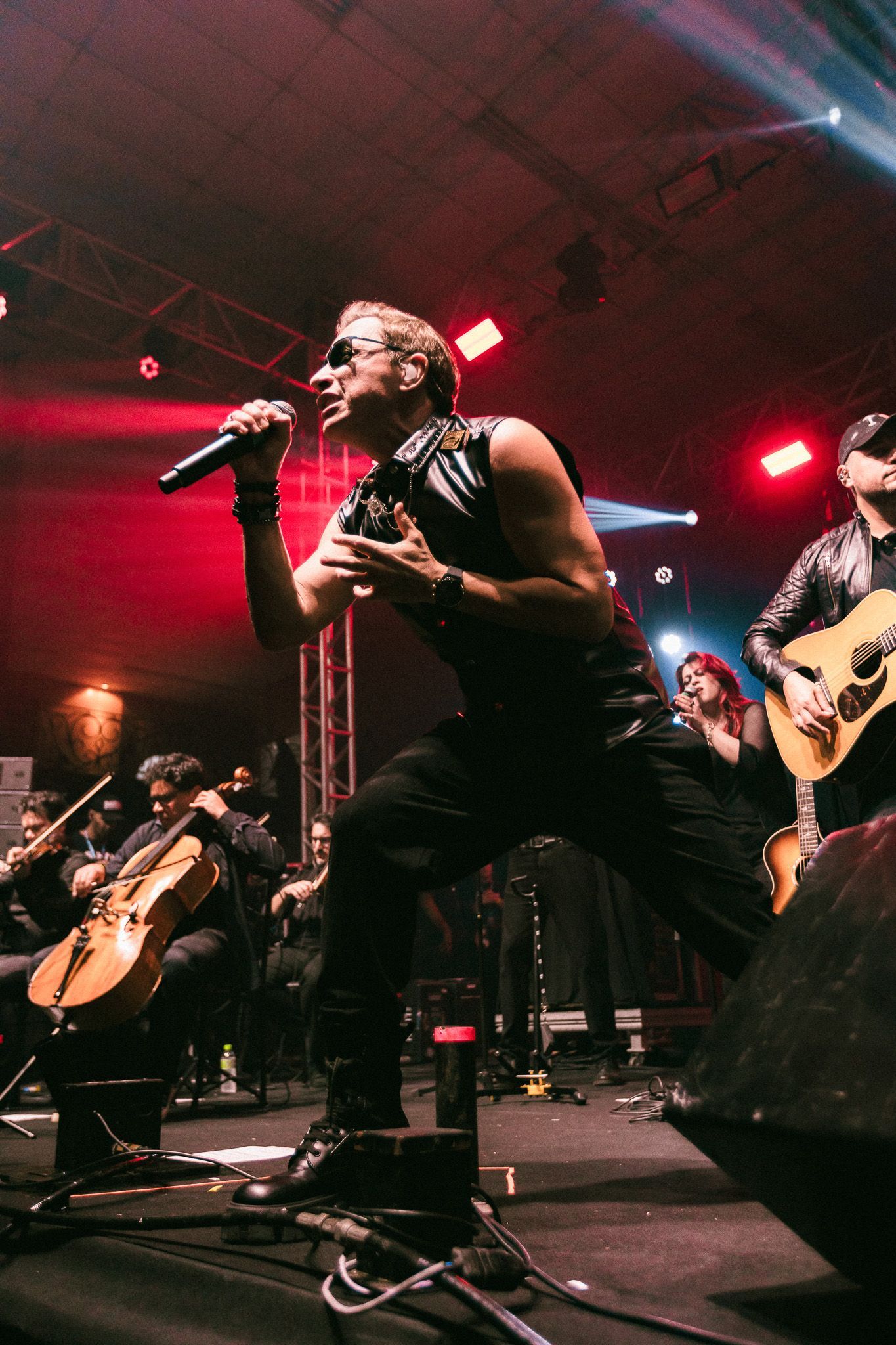 Cantor no palco com a banda, iluminação de palco vermelha e azul.