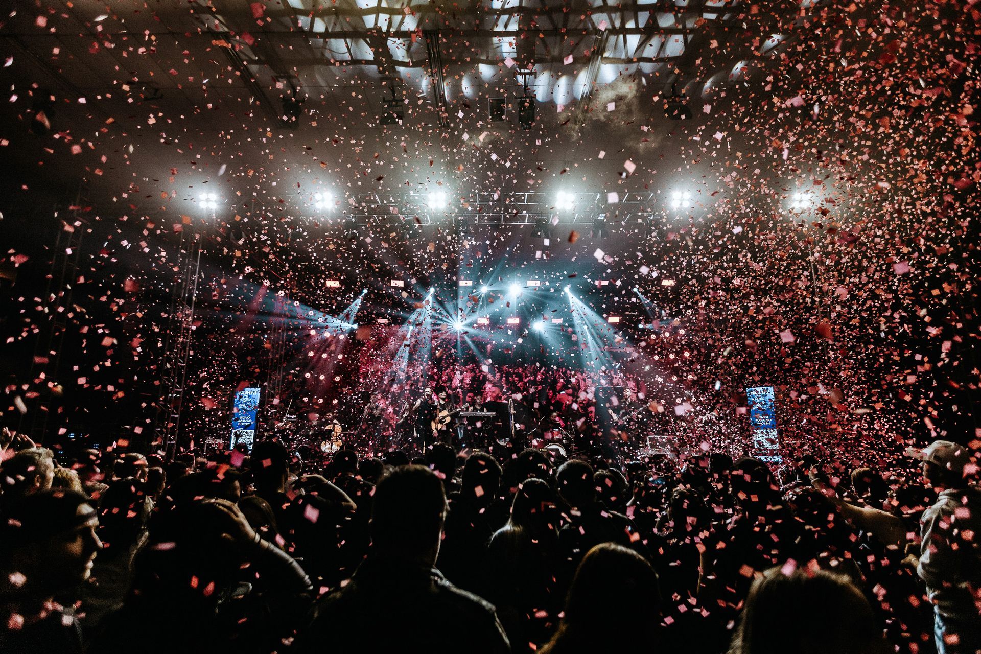 Concerto com chuva de confetes e luzes do palco iluminando a multidão.