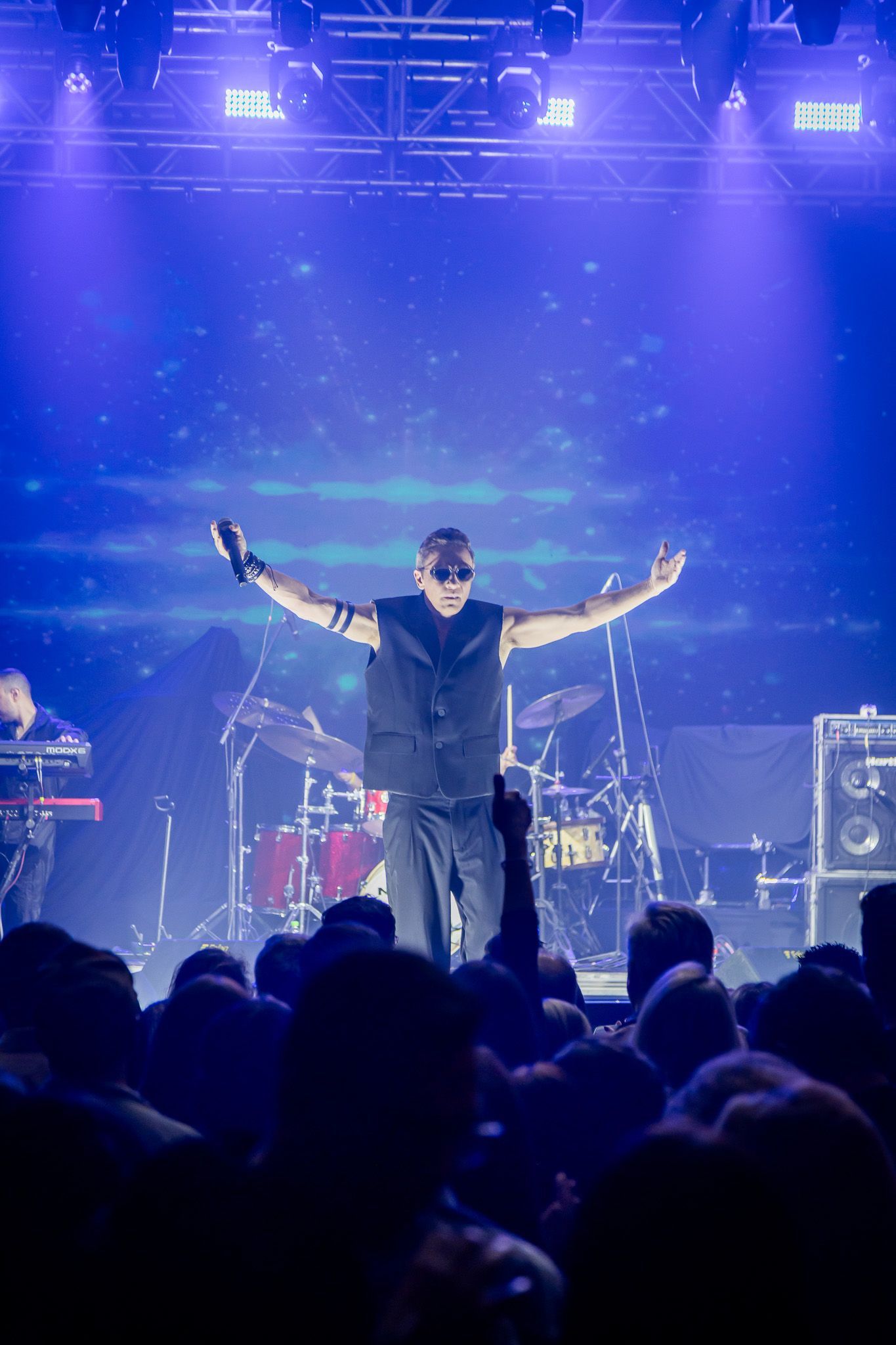 Um artista com os braços estendidos está em um palco banhado por luz azul diante de uma grande plateia.