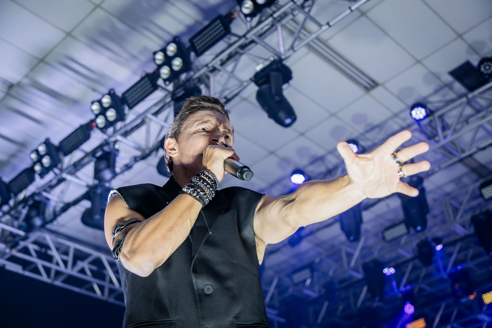 Um cantor se apresentando no palco, segurando um microfone em uma das mãos e estendendo a outra para a plateia.