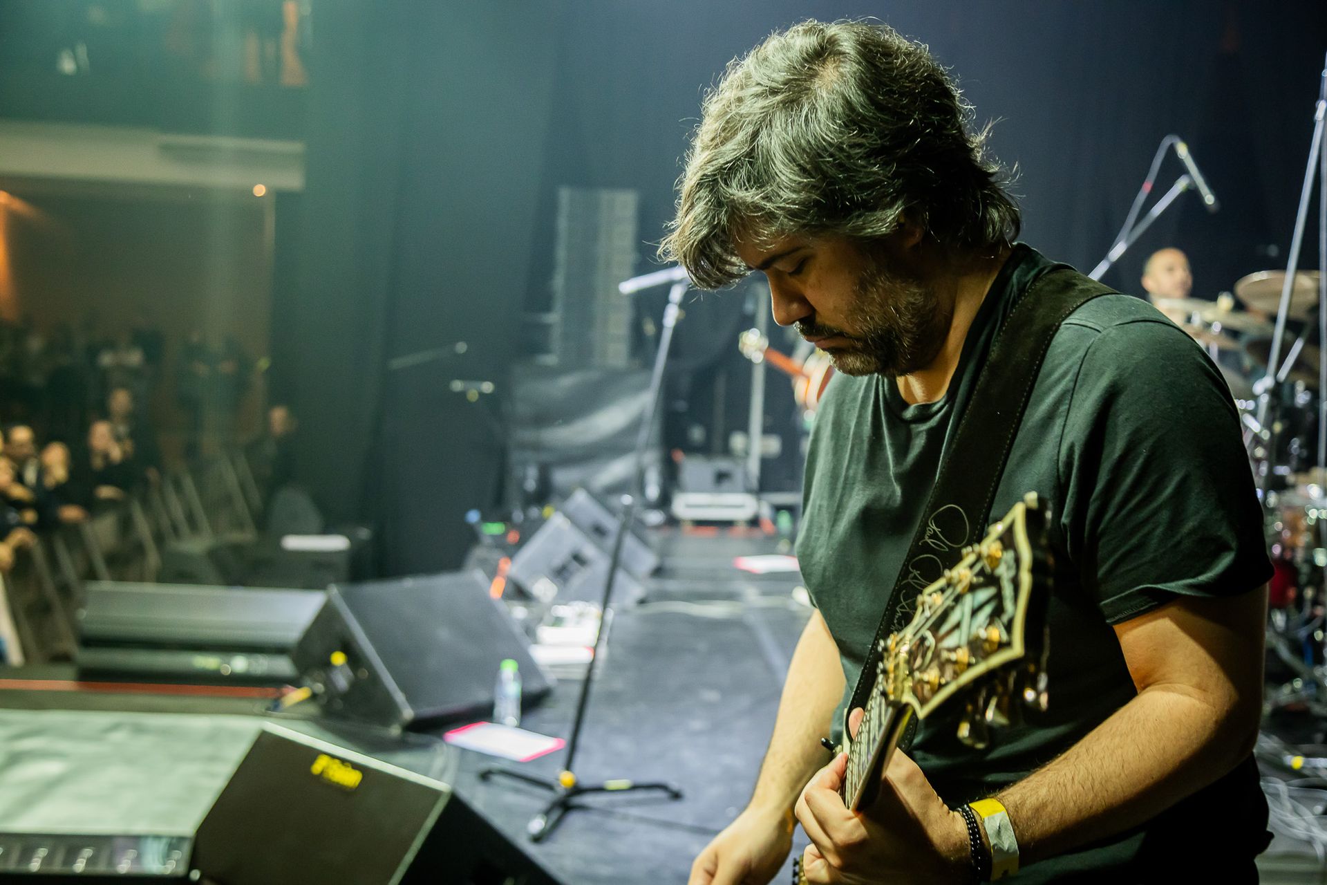 Um músico se apresenta em um palco de concerto, tocando guitarra elétrica enquanto olha para o instrumento.