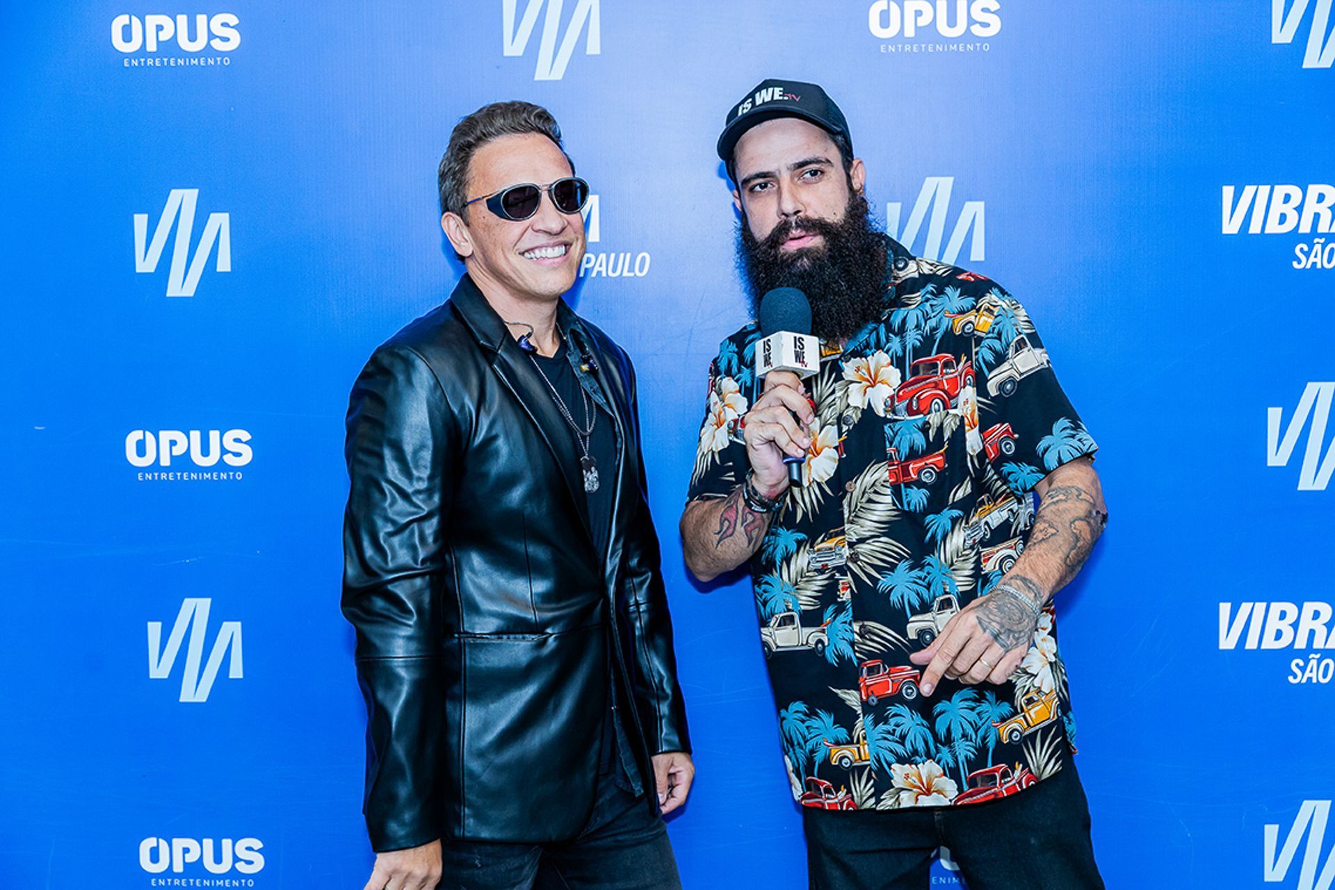 Dois homens posam contra um fundo azul com logotipos de eventos; 